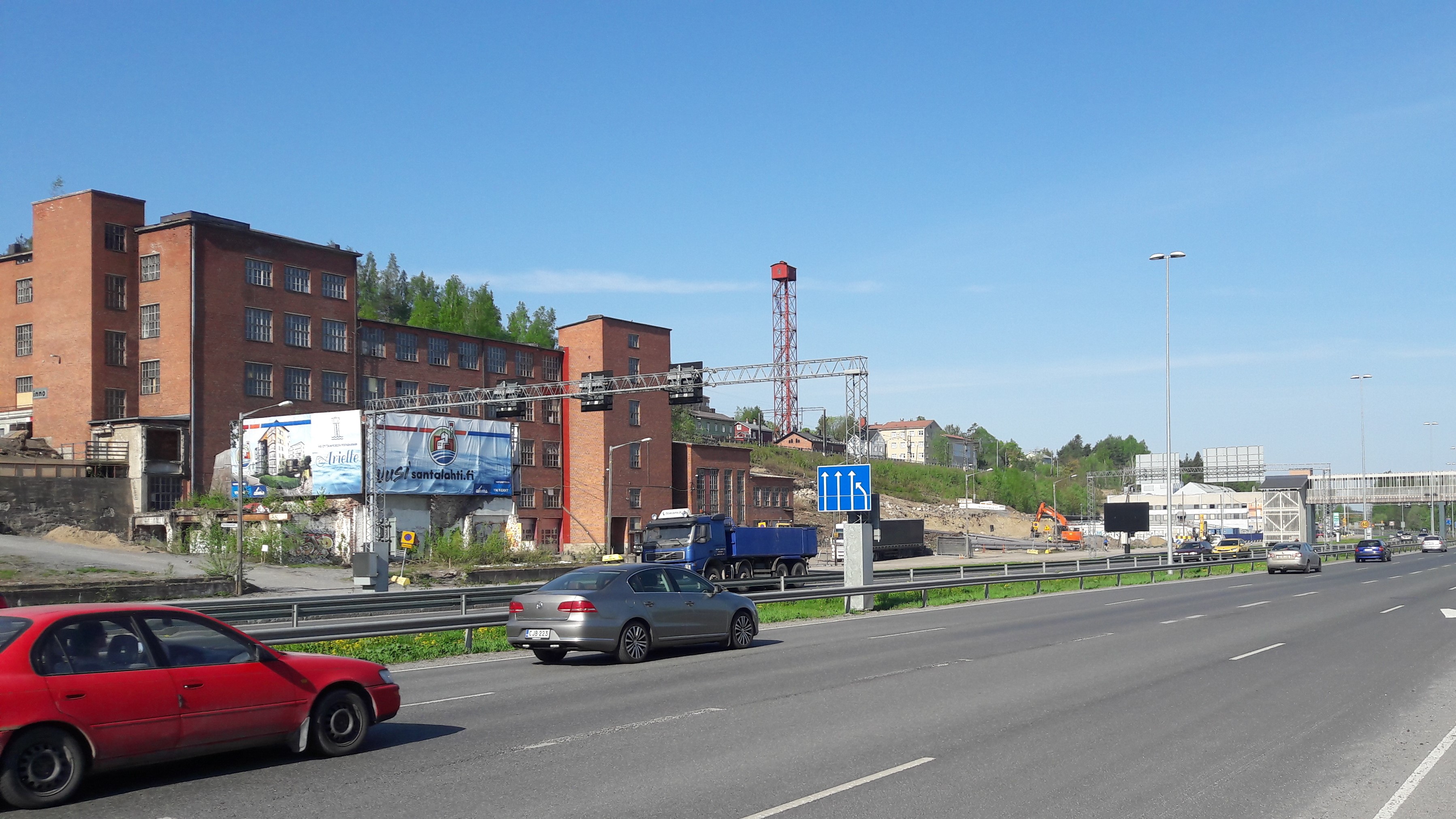 Etualalla autotie ja sen vieressä vanha, tiilinen teollisuusrakennus. Taustalla kohoaa harju.