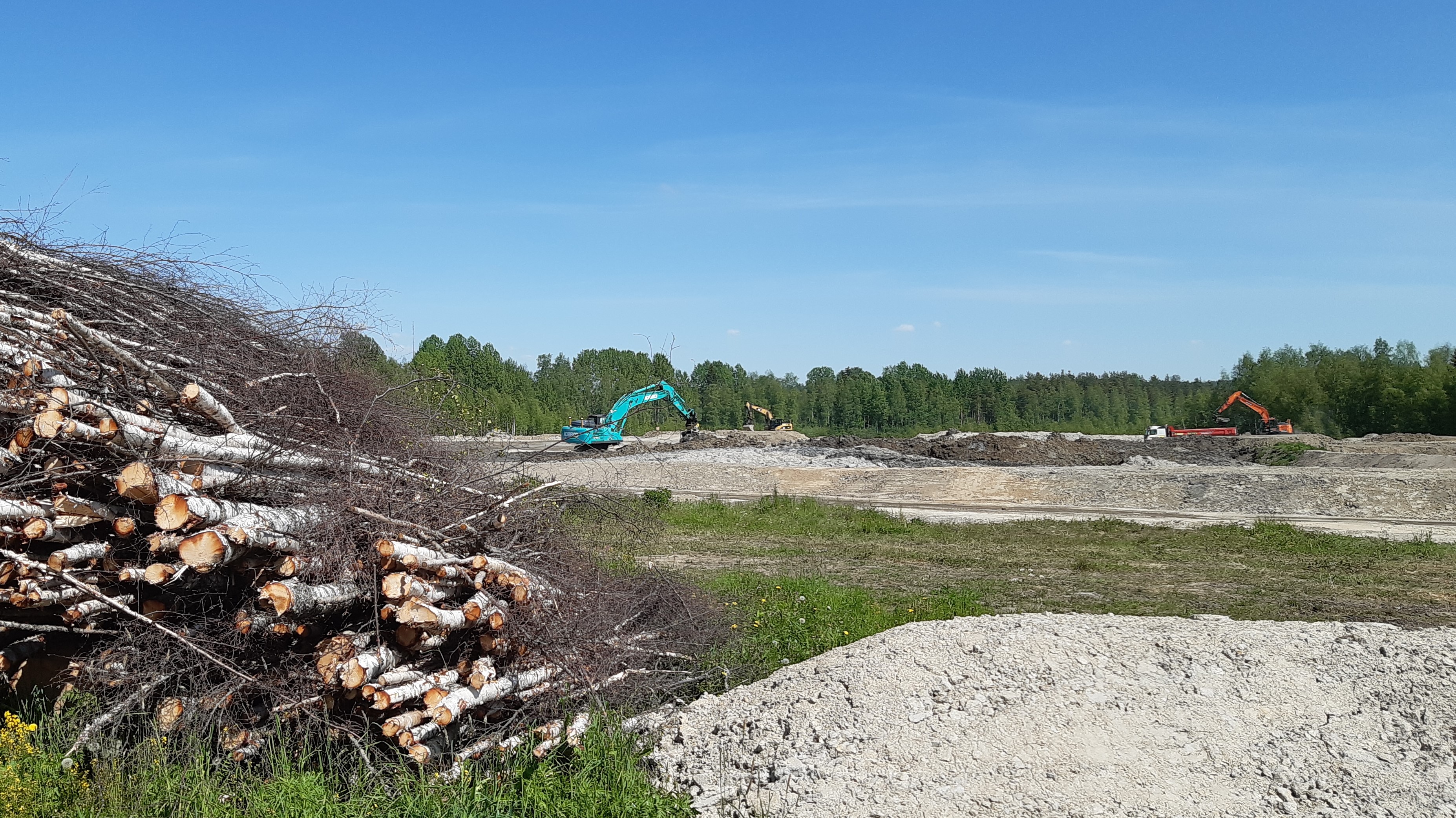 Etualalla nipussa kaadettuja puita, taaempana kaivuualueta ja kaksi kaivinkonetta, niiden takana metsää.