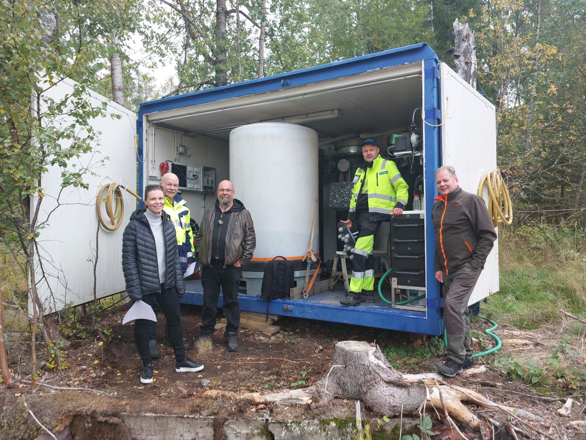 Ihmisiä hymyilemässä kameralle kontin edessä.