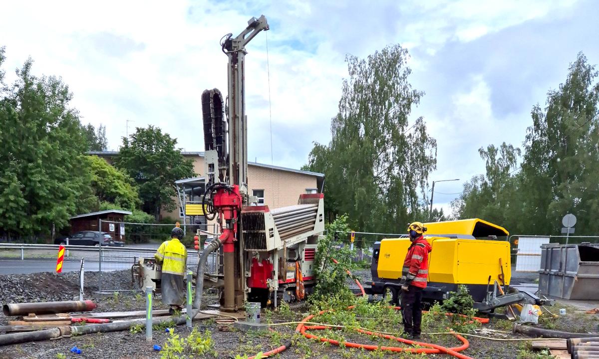Kuvassa on työkone työmaalla ja kaksi työntekijää.