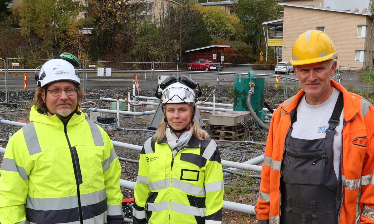 Kuvassa on taustalla työmaa ja kolme ihmistä turvavarusteissa.