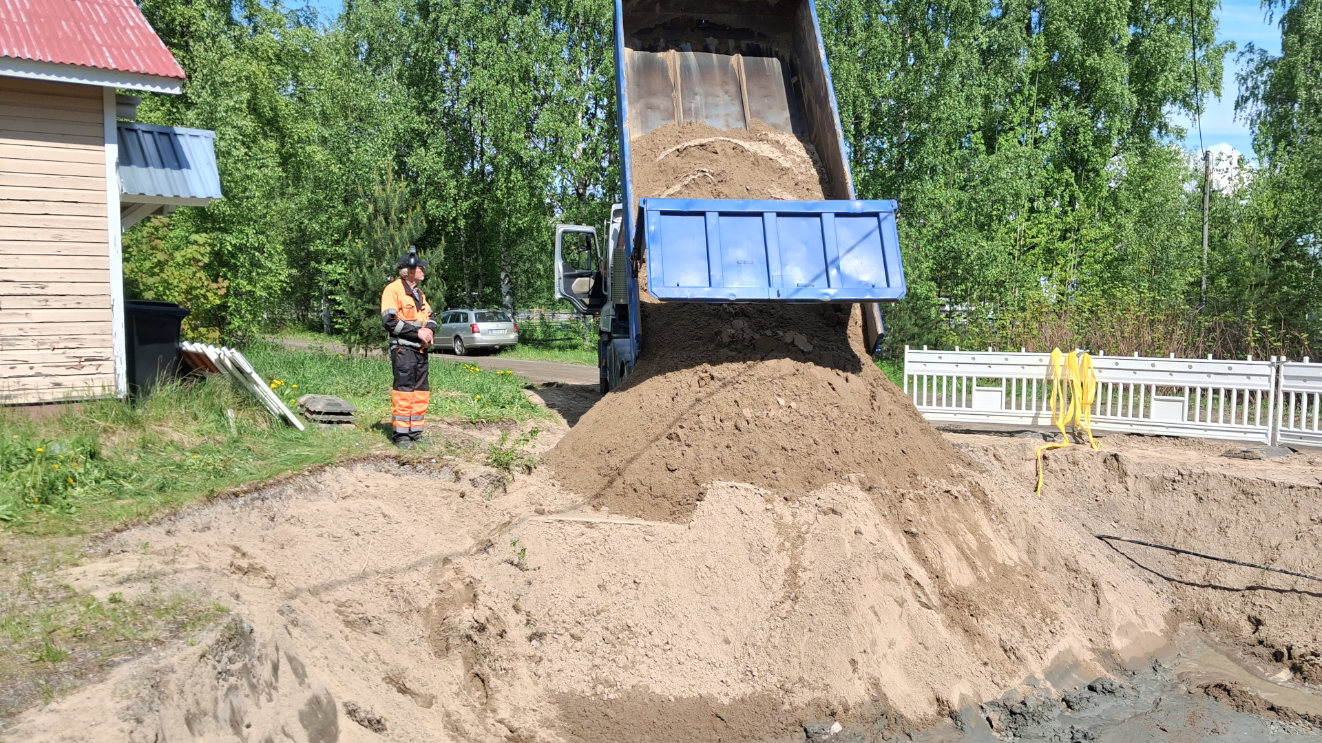 Kuvassa on on henkilö ja kuorma-auto, josta kipataan maata kaivantoon. 