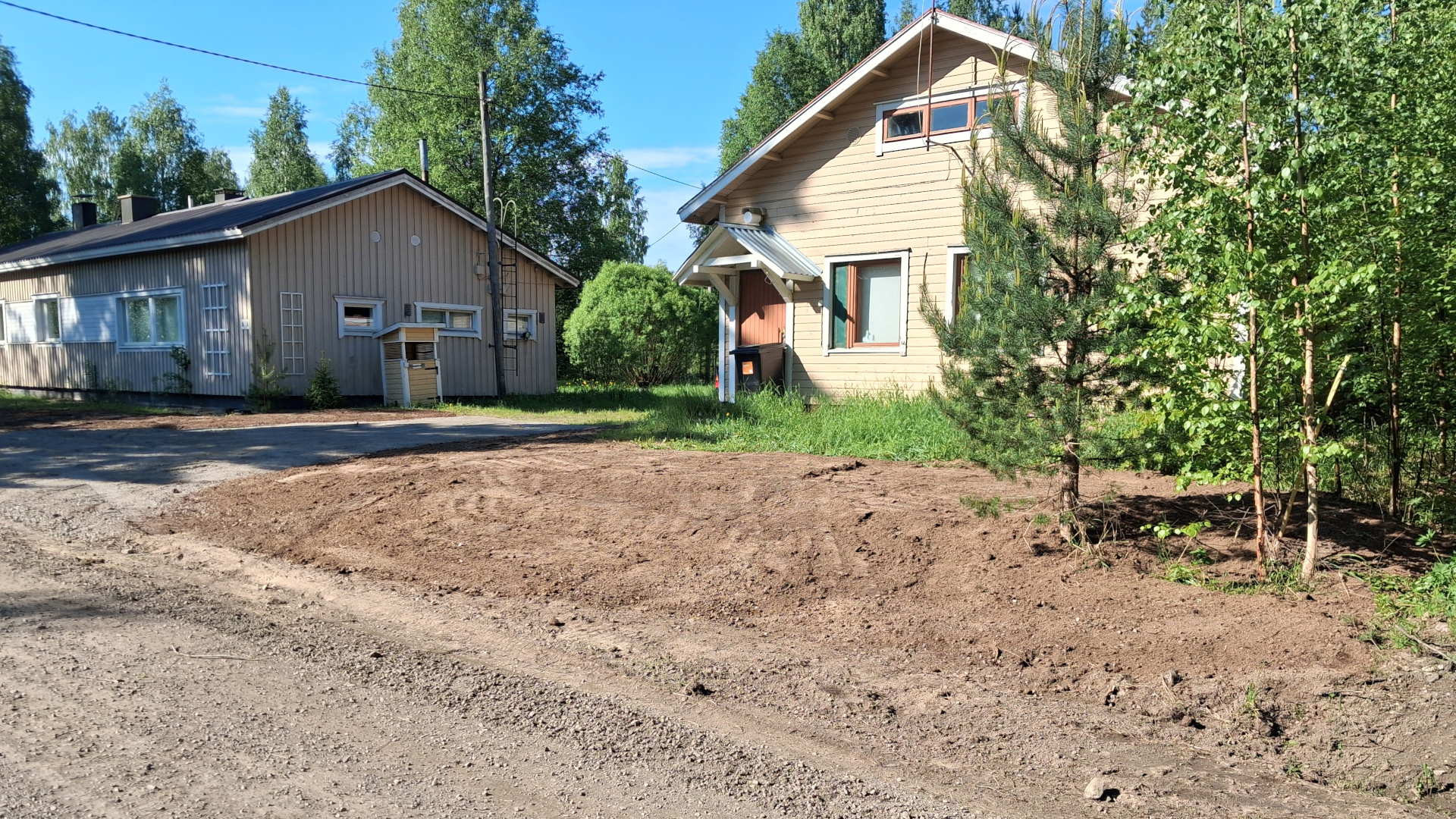Kuvassa näkyy kaksi rakennusta, tietä ja alue, johon puhdas maa-aines on levitetty.